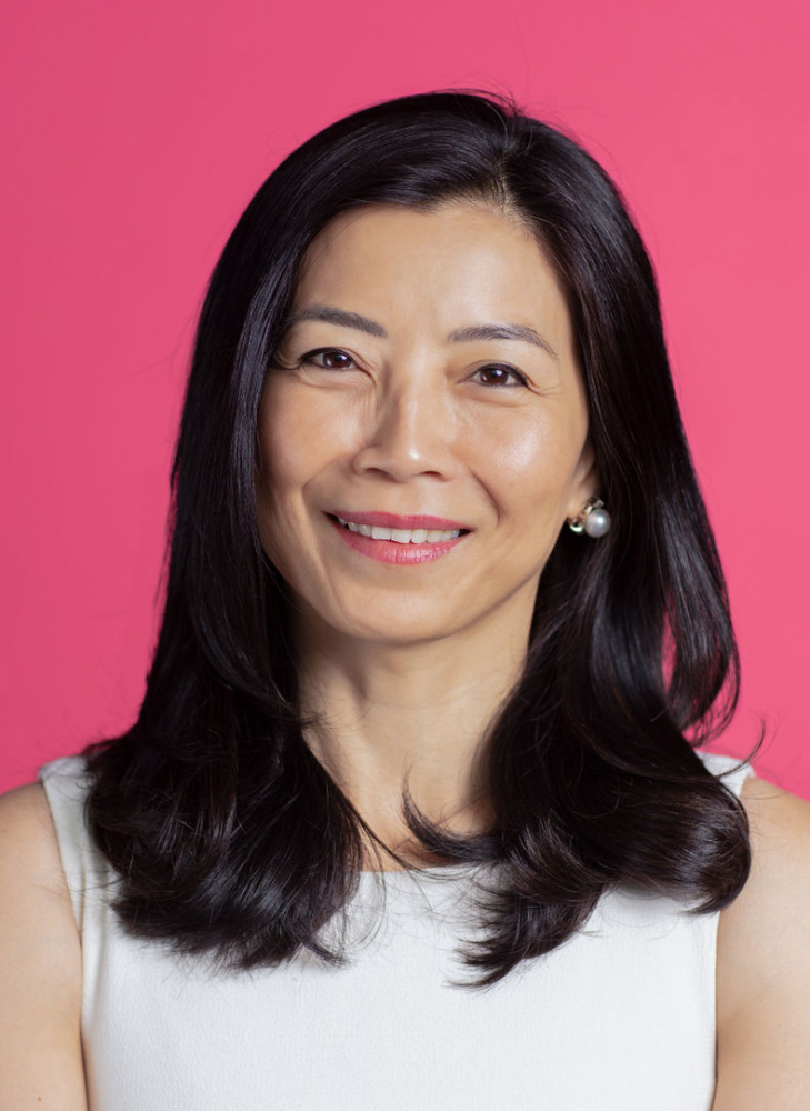 Tracy Palandjian, an asian woman, smiling in front of a pink background.